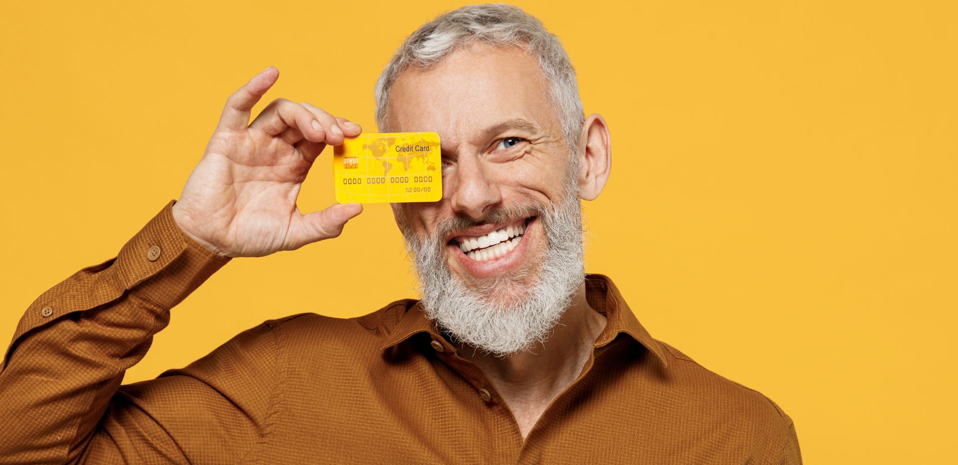 Uśmiechający się mężczyzna z siwą brodą trzymający kartę kredytową