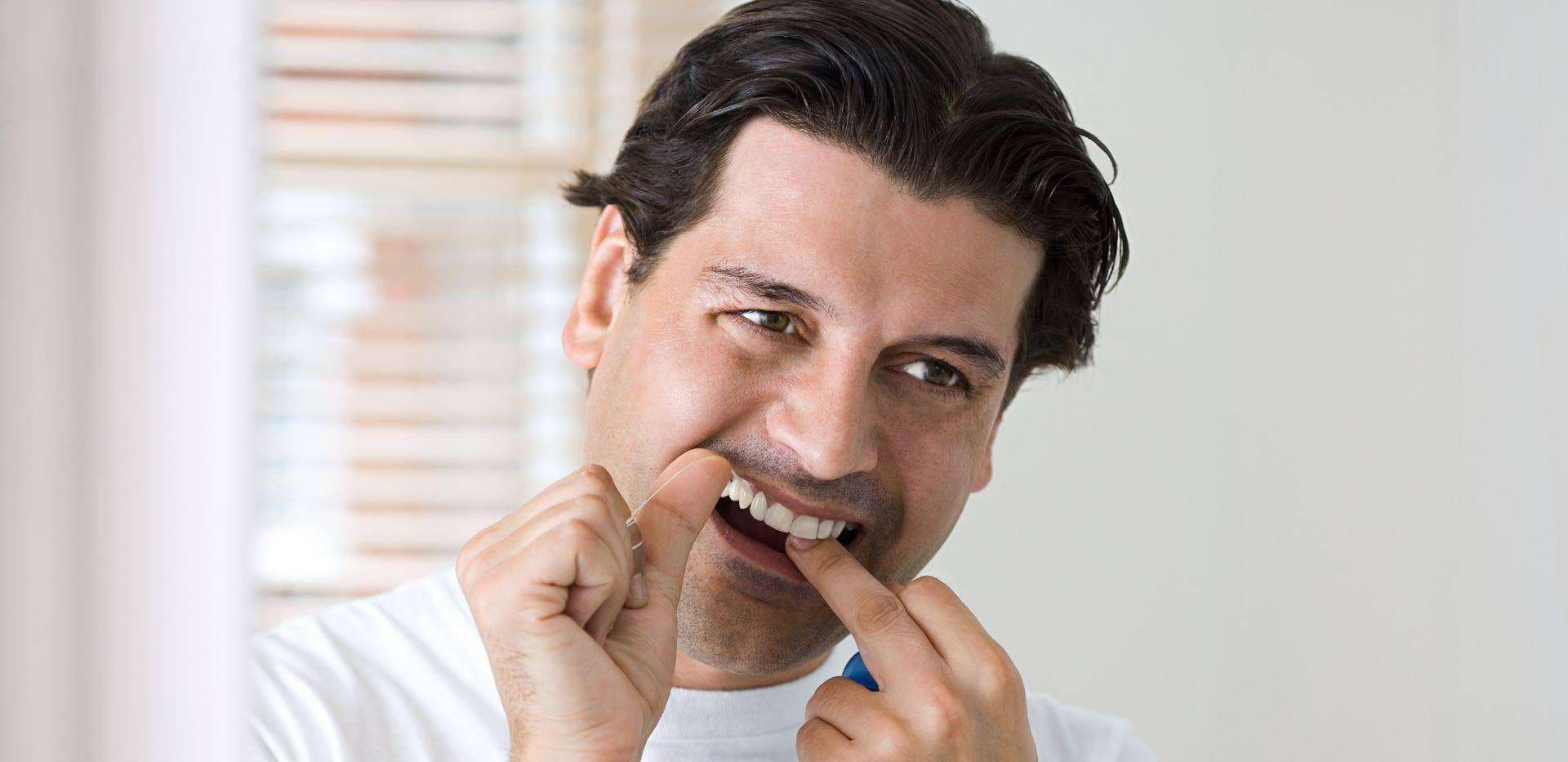 Muž čistiaci si medzizubné priestory dentálnou niťou.