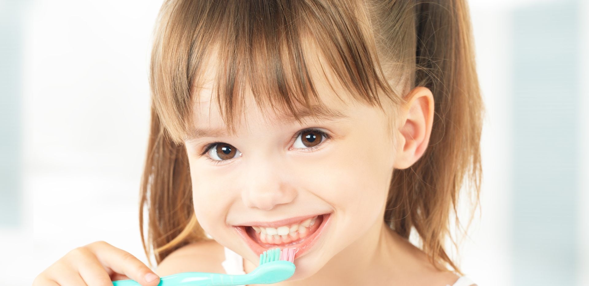 Úsměv malé dívky čistící si zuby modrým zubním kartáčkem.